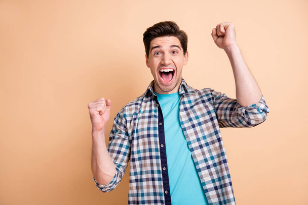 Portrait of nice cheerful overjoyed guy wearing checked shirt having fun rejoicing isolated over beige pastel color background - Foto, imagen