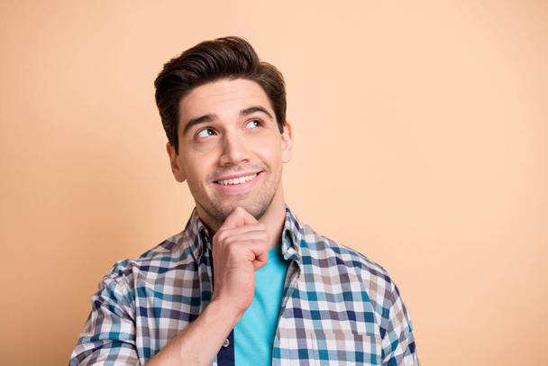 Close-up portrait of nice minded cheery guy touching chin thinking copy space wearing checked shirt isolated over beige pastel color background - Foto, imagen