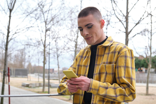 Young non binary person checking his smartphone and smiling. Make up androgynous person. - Photo, image