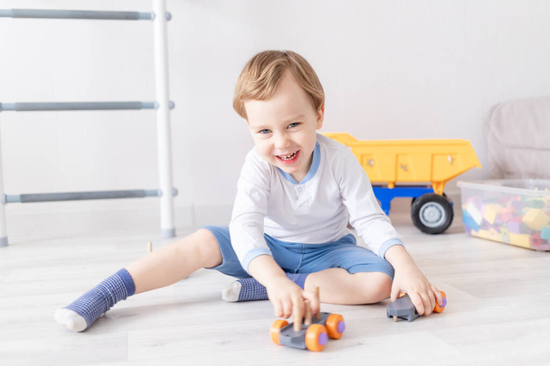 мальчик играет с деревянными игрушками дома на полу - Фото, изображение