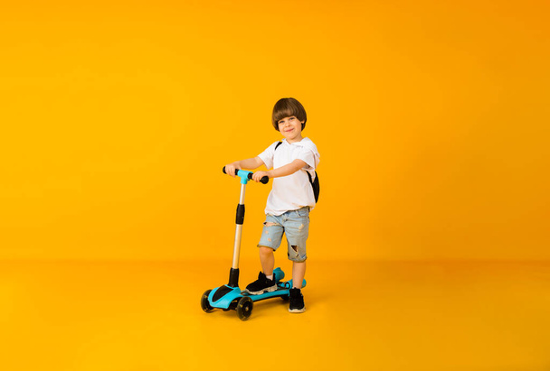 маленький мальчик катается на скутере на желтом фоне с местом для текста - Фото, изображение