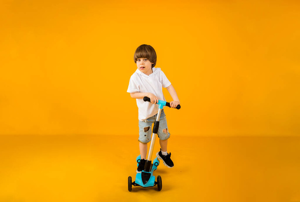 happy little boy riding a scooter on a yellow background with space for text - Φωτογραφία, εικόνα