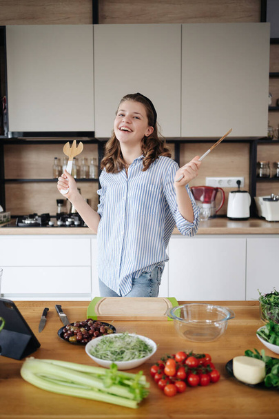Χαρούμενο κορίτσι που χορεύει ενώ μαγειρεύει κρατώντας τα χέρια ψηλά - Φωτογραφία, εικόνα