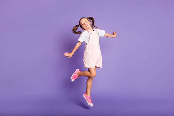 Full body photo of dreamy positive little girl jump up air wear pink shoes isolated on purple color background - 写真・画像