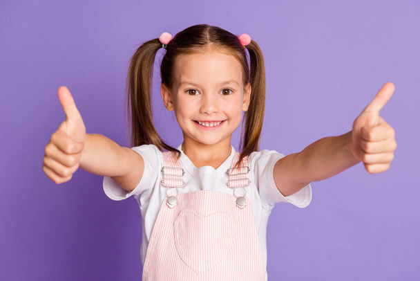 Photo of happy little girl make two thumbs up charming smile recommend isolated on purple color background - Фото, изображение