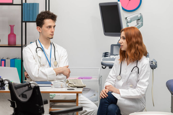 A young doctor talks to a redheaded intern about his next patient. GP. Doctors office - Photo, image
