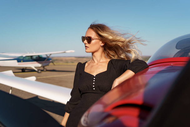 Прекрасная женщина в солнечных очках позирует рядом с самолетом - Фото, изображение
