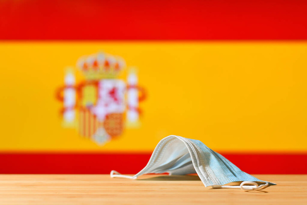 Una maschera medica si trova sul tavolo sullo sfondo della bandiera della Spagna. Il concetto di un regime di maschera obbligatoria per i residenti del paese e turisti in Spagna durante una pandemia. - Foto, immagini