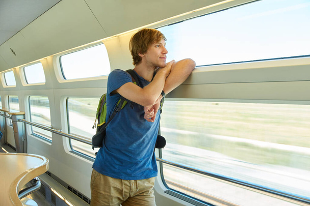 man with a backpack riding by train. traveler on the road looking out the window. - 写真・画像