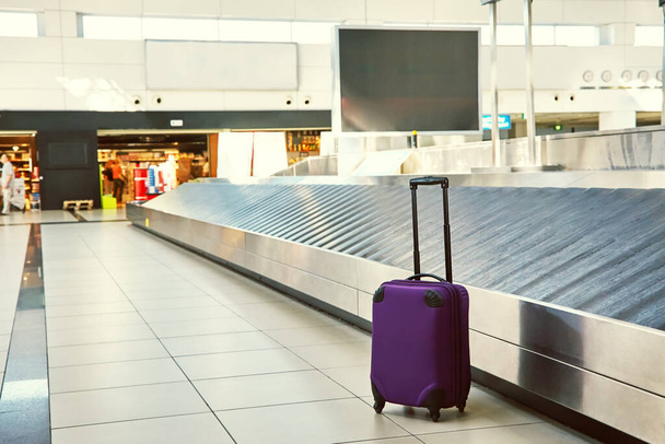 suitcase standing near empty conveyor belt at baggage claim at airport. - Fotó, kép