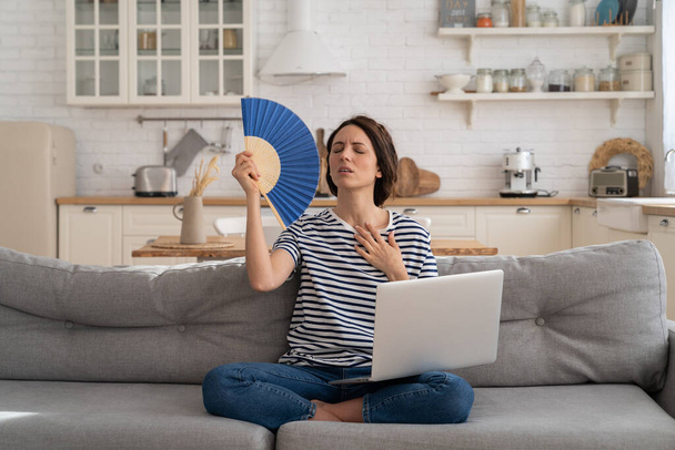 Nuori nainen kärsii lämpöhalvaus tasainen ilman ilmastointilaite heiluttaa tuuletin istuu sohvalla kotona - Valokuva, kuva
