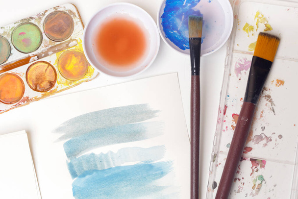 Aquarellfarben Palette, Pinsel und Papiere auf dem Tisch. Kreatives Hobby- oder Kunsttherapiekonzept. - Foto, Bild