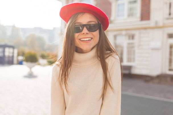 Onnellinen viehättävä eurooppalainen tyttö, jolla on pitkät hiukset aurinkolasit ja baskeri hymyillen kameralle auringonvalossa. Laadukas kuva - Valokuva, kuva