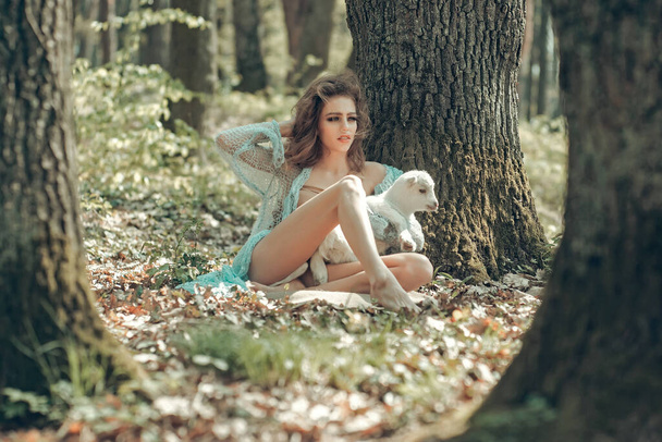 Young woman holding cute white small goat in sunny forest. - Fotoğraf, Görsel