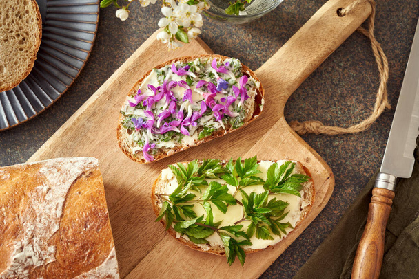 Дві скибочки хліба з дикими їстівними весняними рослинами - подрібнене старе листя, фіолетові мертві квіти та квіти, придатні для перемішування
 - Фото, зображення