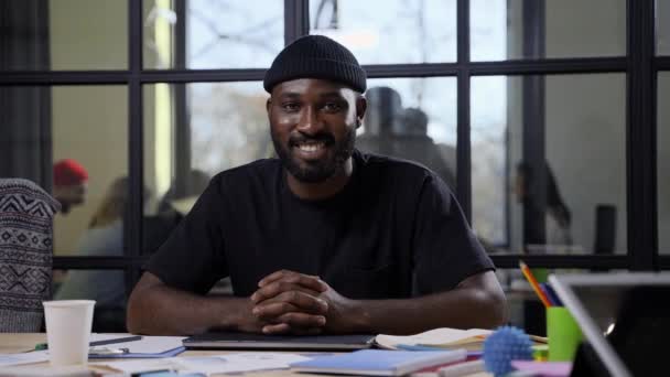 Uśmiechnięty Afroamerykanin pozujący na stanowisku pracy - Materiał filmowy, wideo