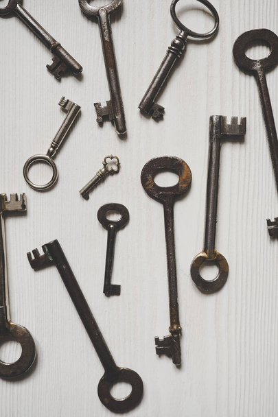 Different old fashioned keys on a white table from above, background - Foto, Imagen
