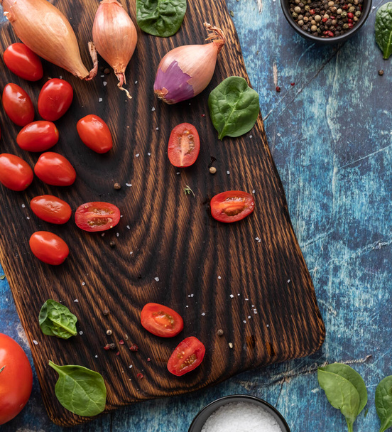 Vista de cima para baixo de uma tábua de corte de madeira com tomate cereja fatiado e chalotas. Cultura Instagram. - Foto, Imagem