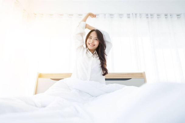 Piękne kobiety azjatyckie budzą się rano w sypialni. Rozciąga się i czuje się świeżo. - Zdjęcie, obraz