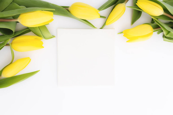 Flat lay with yellow tulip flowers and empty picture frame on white background. Greeting card design for Easter, Mothers day, International womens day or Saint Valentines day - Foto, Bild