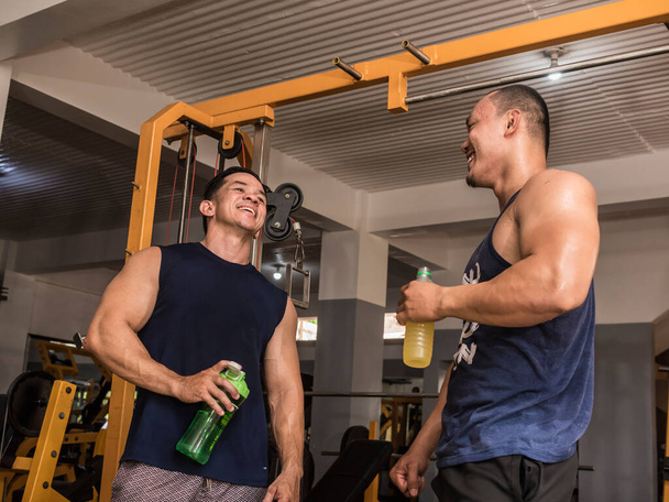Zwei Bodybuilder unterhalten sich nach einer Trainingseinheit freundlich. Beide mit einem Erholungsgetränk nach dem Training. - Foto, Bild