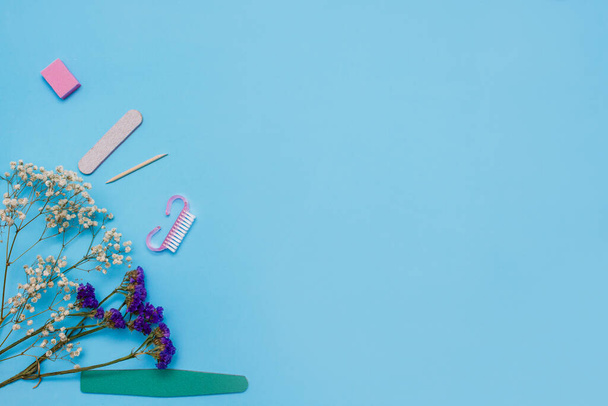 Manicure tools on a blue background are decorated with white gypsophila flowers. The concept of beauty. Copy space. top view. - 写真・画像