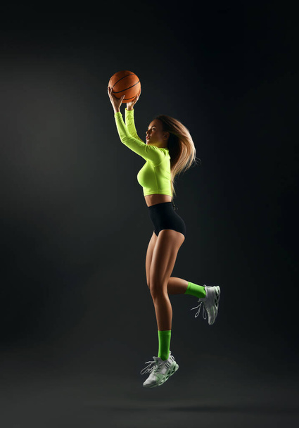 Basketball woman player jumps and throws ball. Tight sportwear black shorts, yellow top with sleeves, socks, sneakers - 写真・画像