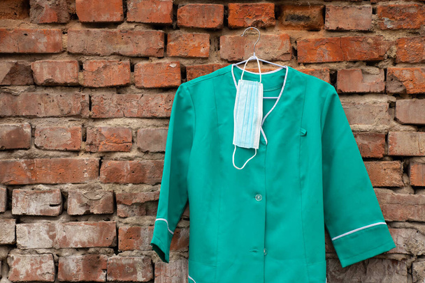 viejo traje médico colgando de una percha en la pared en la calle en Ucrania, uniforme de enfermera - Foto, Imagen