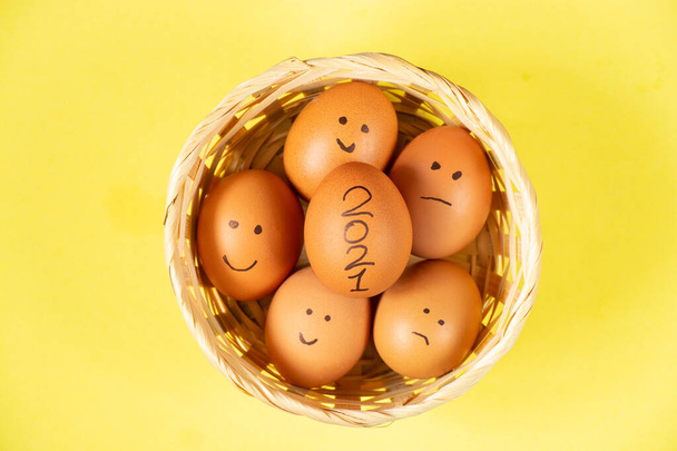 ζωγραφισμένα emoticons σε αυγά κοτόπουλου και 2021 που βρίσκονται σε ένα ψάθινο καλάθι σε ένα απομονωμένο κοντινό πλάνο - Φωτογραφία, εικόνα