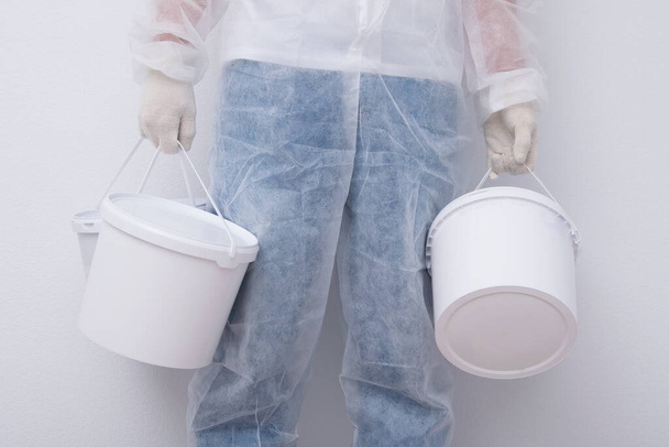 a man in protective clothing, bringing buckets of paint, against a white wall, close-up - Фото, изображение