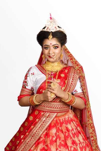 Stunning Indian bride dressed in red traditional Banarasi sari embroidered with gold jewellery and bangles holding gach kouto or sindoor box in front of white background. Ethnic wedding and fashion. - Photo, Image