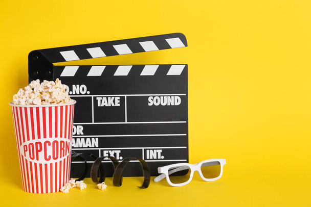 Delicious popcorn, 3D glasses, tape and clapperboard on yellow background - Fotografie, Obrázek