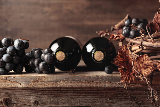 Lahvičky červeného vína s hrozny a sušenou révou na starém dřevěném stole. Kopírovat prostor. - Fotografie, Obrázek