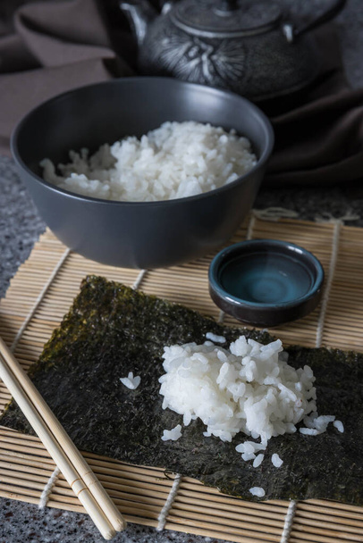Rotolo di sushi giapponese fatto in casa. Ingredienti per fare il sushi roll a casa. Una ciotola nera di riso e teiera nera .  - Foto, immagini