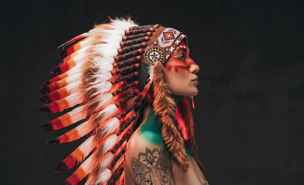 Tetovált trendi nő, tollas nemzeti fejfedőt visel - Fotó, kép