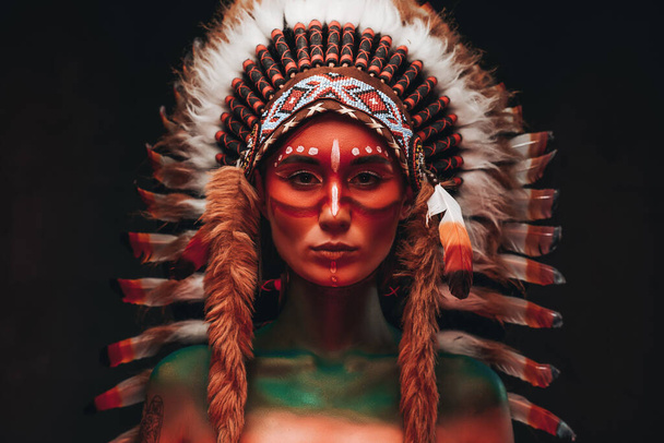 Tribal woman warrior with headwear from feathers in dark background - Photo, Image
