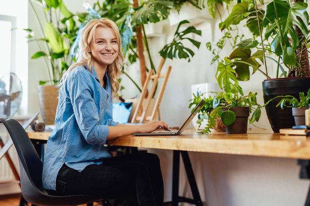 Joyful female business person works on her laptop in office with plants - 写真・画像
