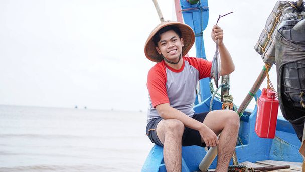 Happy young fisherman on the beach holding his catch fish and shows in front of his boat - Foto, Imagem