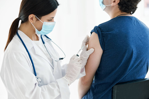 een verpleegkundige injecteert een vaccin in de schouder van een patiënt met een medisch masker - Foto, afbeelding