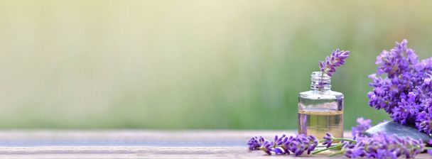 panoraamanäkymä pullo eteerinen öljy ja laventeli kukkia järjestetty puinen pöytä sumealla taustalla  - Valokuva, kuva