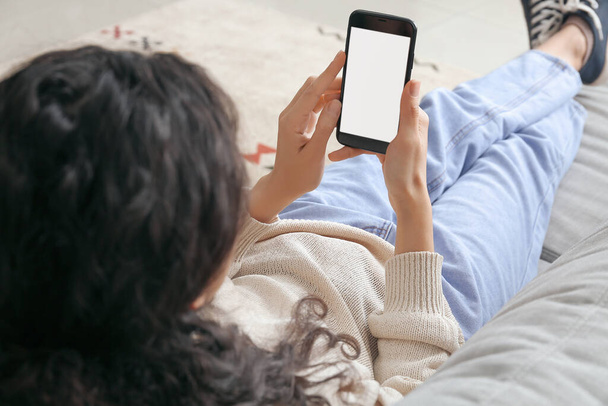 Жінка з мобільним телефоном лежить на дивані в кімнаті
 - Фото, зображення