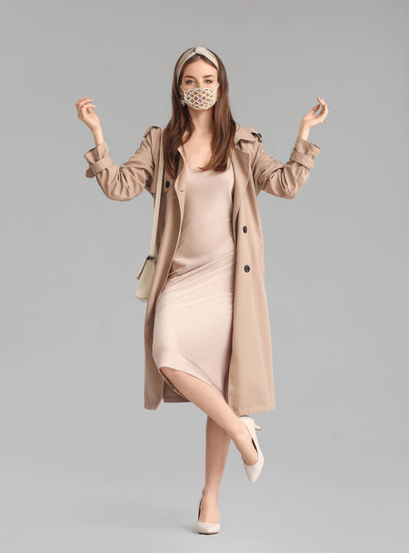 Mujer joven de moda con máscara sobre fondo gris - Foto, Imagen