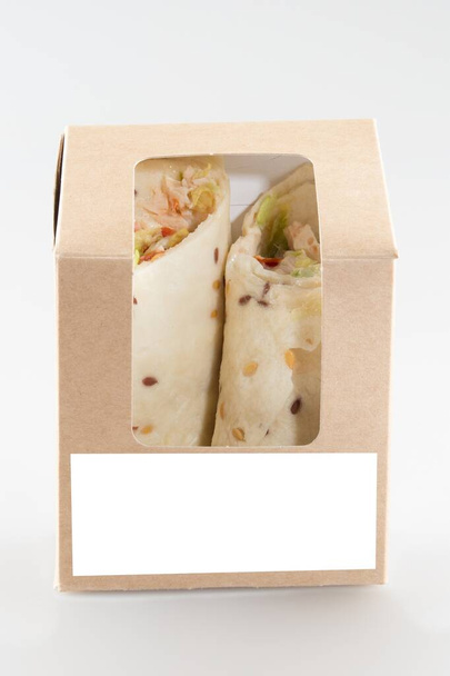 Tortilla envuelve verduras y saliva afeitada asada en caja de cartón marrón con papel de hoja en blanco para el texto maqueta de espacio en blanco vacío para la marca del logotipo aislado en el fondo - Foto, Imagen