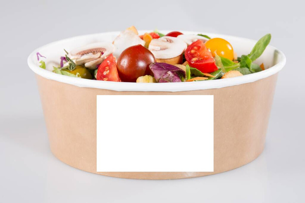Lleve la caja de ensaladas lista para vegetarianos con papel de hoja en blanco para texto maqueta de espacio en blanco vacío para la marca del logotipo aislado sobre fondo de mesa gris - Foto, Imagen