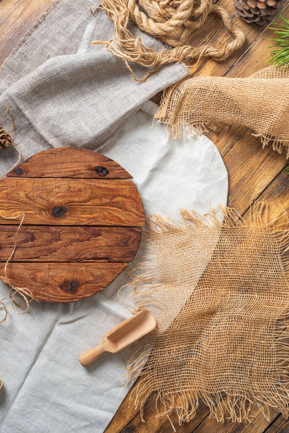 Fragmento de uma tábua de corte de madeira redonda feita de tábuas ásperas em linho e tecido folgado. Cones, uma corda, uma colher de nozes estão nas proximidades.  - Foto, Imagem