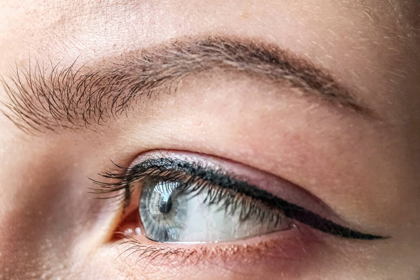 Ojo femenino de color azul de una joven de cerca. Maquillaje permanente del ojo y de la ceja para los párpados y las cejas. - Foto, imagen