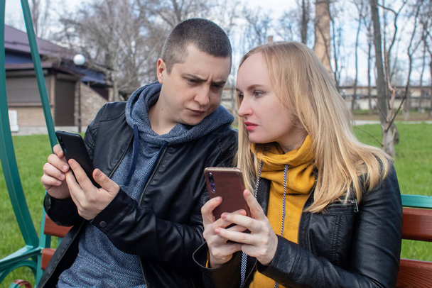 Homme et une femme sont tous les deux assis sur un rendez-vous et siroter dans leurs smartphones. Concept de dépendance aux médias sociaux, sortir de la réalité et s'ignorer mutuellement. Couple assis sur une balançoire dans le parc - Photo, image