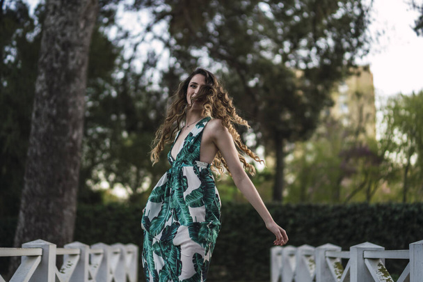 A shallow focus shot of a beautiful Spanish Caucasian woman with curly hair, posing on a wooden bridge while wearing a green dress - Zdjęcie, obraz