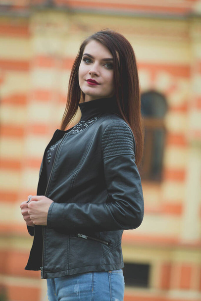 A vertical shot of a young brunette female in a leather jacket posing in a street - Foto, Bild