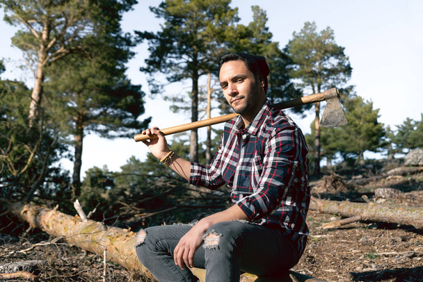 A caucasian lumberman is resting on a wooden log with an ax on his shoulder - Foto, Imagem
